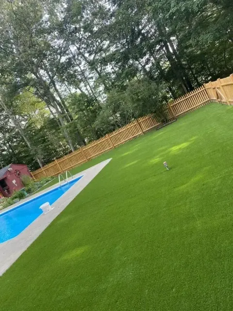 A swimming pool surrounded by an artificial green lawn and a wooden fence.