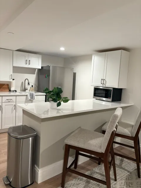 Modern kitchen with white cabinets, stainless steel appliances, and a countertop with two barstools.