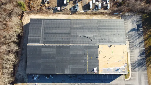Aerial view of a damaged black industrial roof with visible cracks and missing sections.