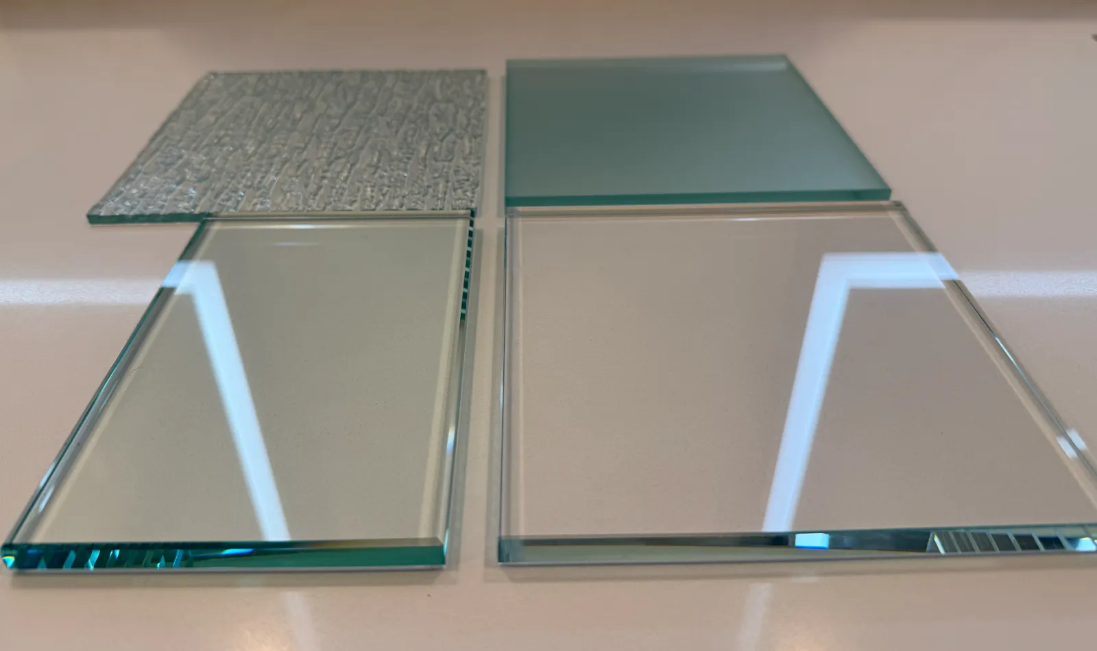 Four glass tiles arranged on a white surface, two with textured surfaces and two with smooth reflective surfaces.