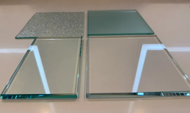 Four glass tiles arranged on a white surface, two with textured surfaces and two with smooth reflective surfaces.
