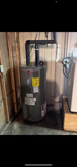 A newly installed water heater standing on a basement floor with its supply lines and venting connected.