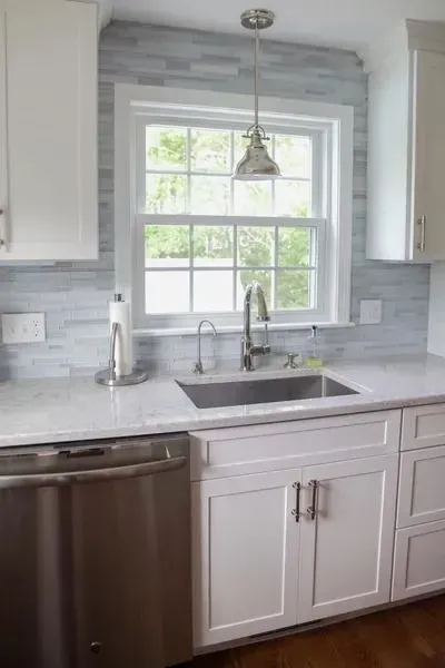 Bright kitchen sink under a window, with white cabinets and stainless steel dishwasher.