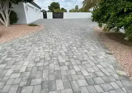 Brick driveway leading to a black gate, bordered by gravel and a white wall.