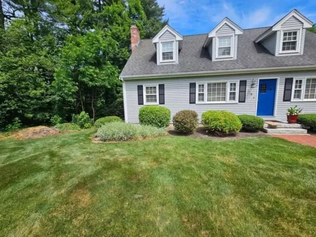 Neat front lawn and trimmed shrubs in front of a grey colonial home with a blue door in Hudson, NH