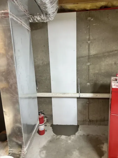 Partially finished utility room with exposed concrete walls, ductwork, fire extinguisher, and white panel.