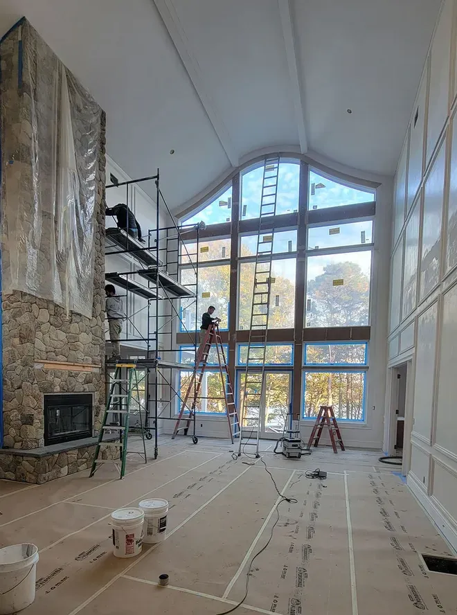 Tall white room under renovation with scaffolding, stone wall, and large arched window wall