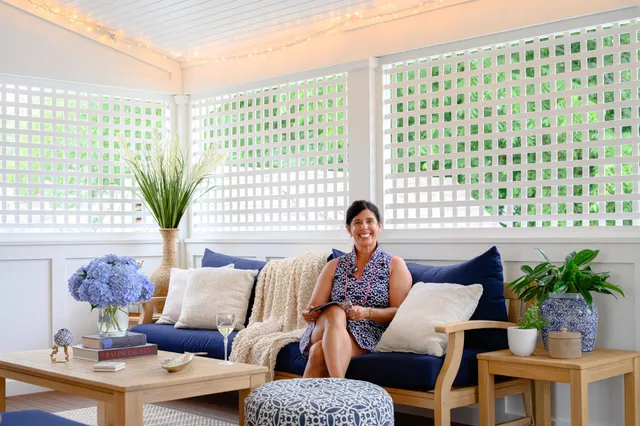 Woman relaxing on a furnished screened porch with blue cushions and string lights