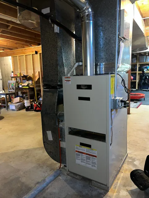 A white furnace is sitting in a basement next to a wall.