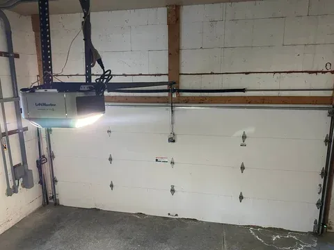 A garage door opener mounted above a white sectional garage door with hardware visible