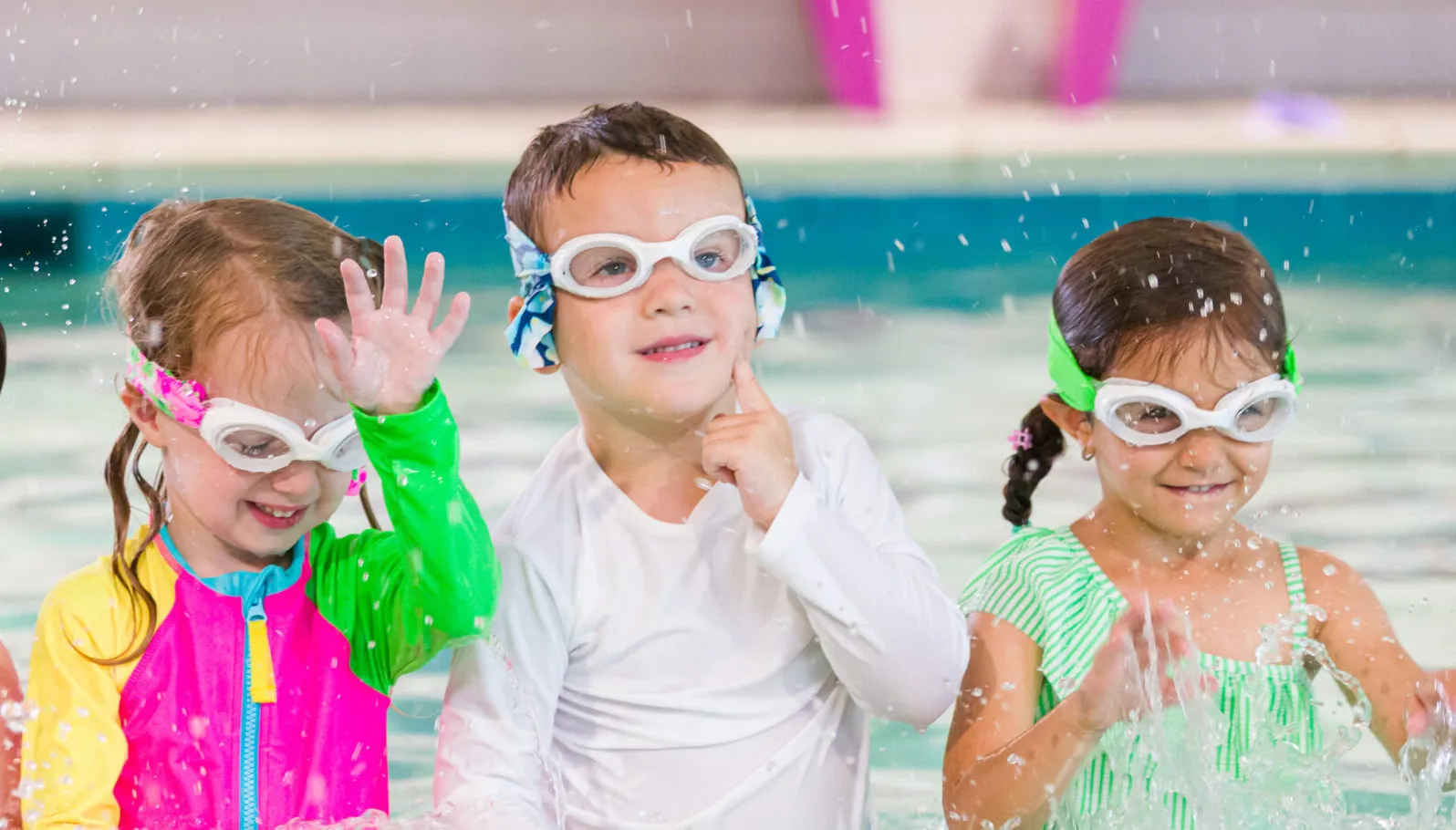 Smiling children participating in preschool swim lessons, wearing goggles and splashing confidently during a safe, instructor-led swim class.