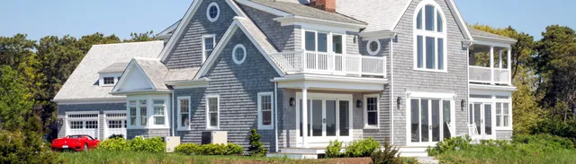large shingled home on the beach with a red car in front on a sunny day