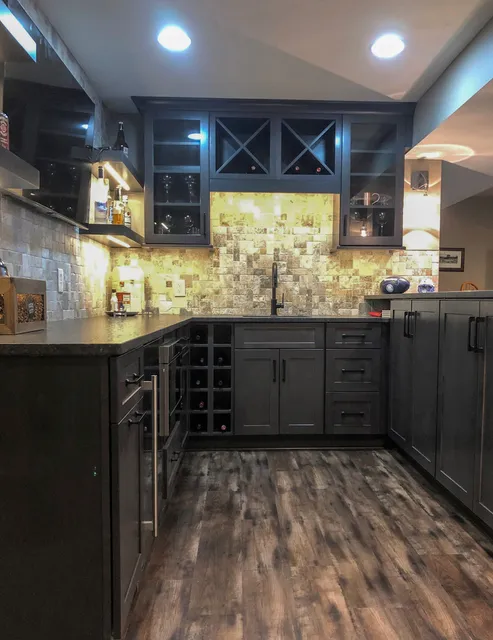 Haute Designs Kitchen & Bath. Bar. Fabuwood Cabinetry – stained cobblestone • Cabinet features: wine storage, trash pull-out, floating shelves, under cabinet lighting. Built-in microwave drawer. Black Hardware Resources hardware. Black wall sconces. Travertine stone backsplash