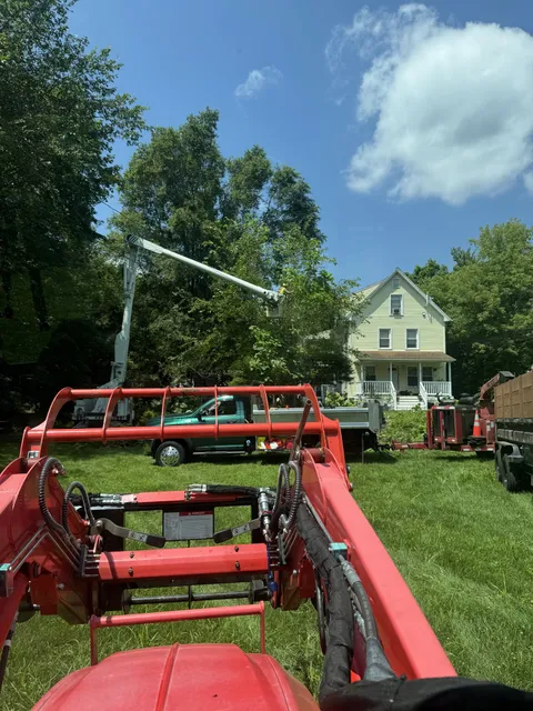 Brush chipper in the foreground with a pickup and bucket truck on the lawn of a white farmhouse