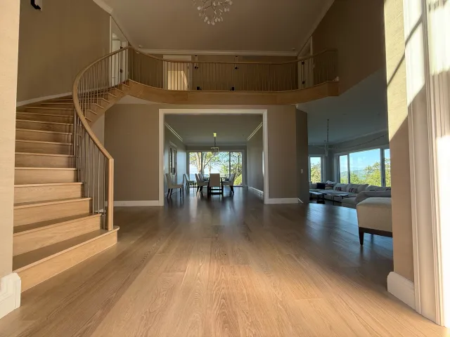 A spacious, multi-level living area with wooden floors, a curved wooden staircase, and a second-floor balcony.