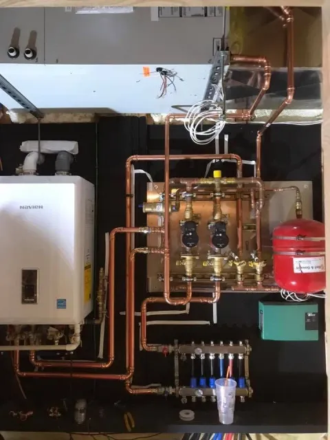 Residential utility room with boiler, copper plumbing, water filter, and red expansion tank installed on the wall