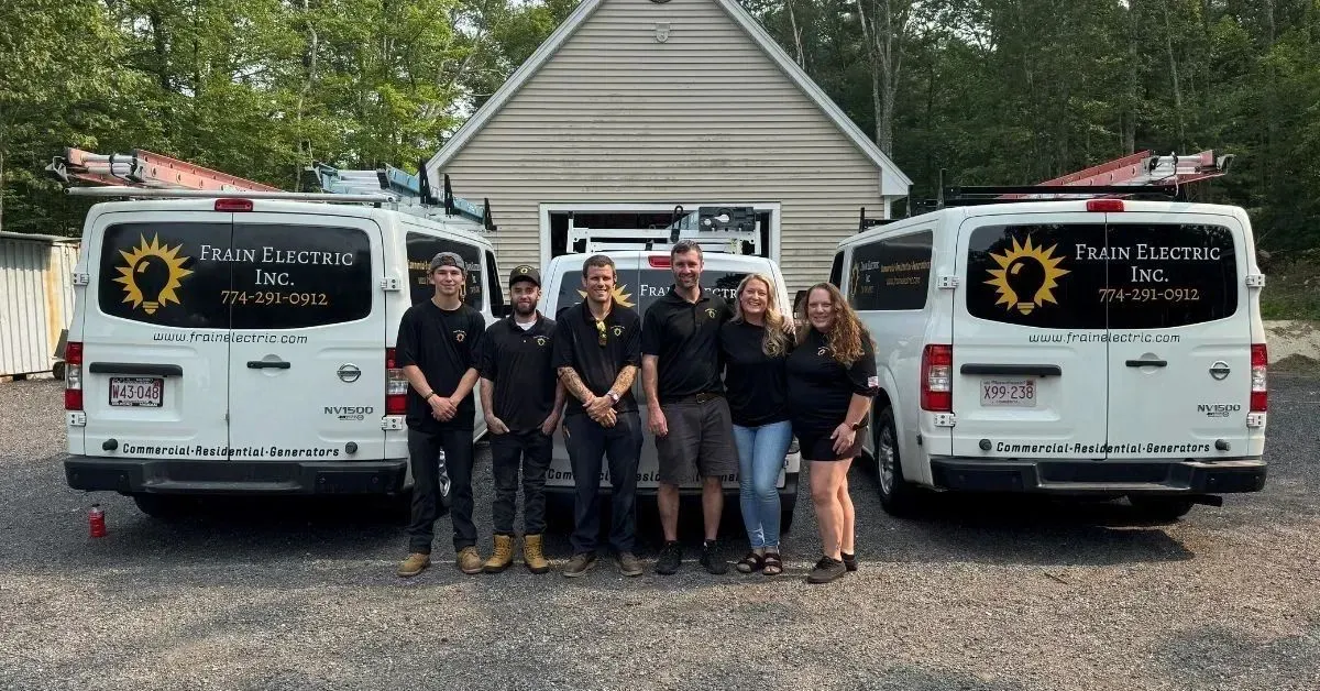 Group of people in front of two white vans with logo, standing in front of a building.