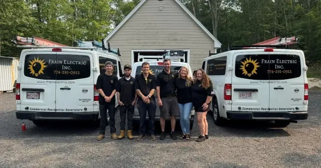 Group of people in front of two white vans with logo, standing in front of a building.