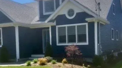 Blue house with white trim and gabled roof, front yard landscaping, and small tree.