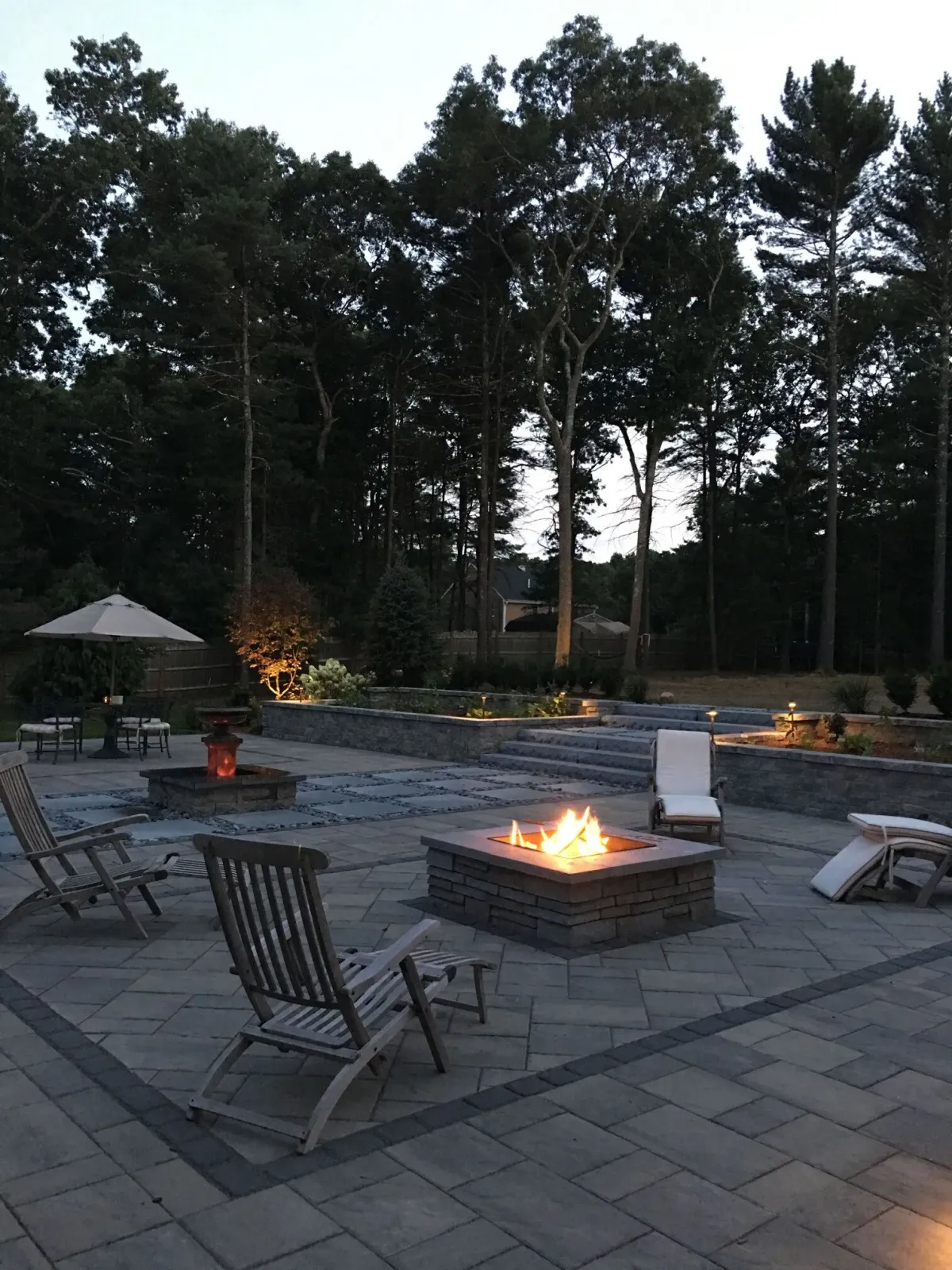 A fire pit on a patio with chairs and umbrellas