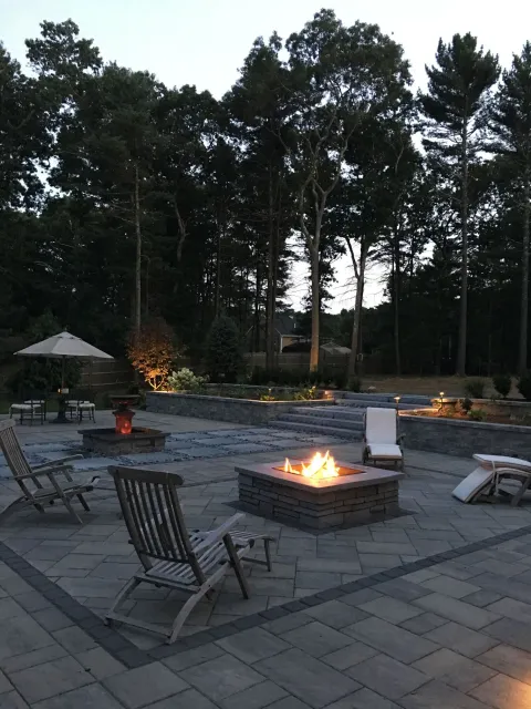 A fire pit on a patio with chairs and umbrellas