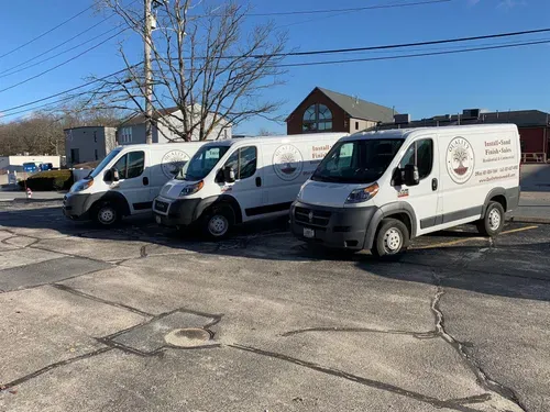 Three white work vans parked on asphalt in front of a building under a clear blue sky.