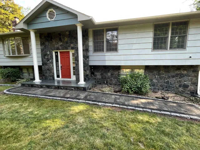 Front view of a house with a red door, white columns, and a stone and siding exterior. There is a paved walkway and lawn in the foreground.