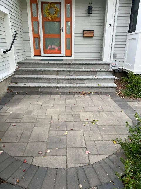 Front steps to a gray house with orange-trimmed double doors and a stone paver walkway.