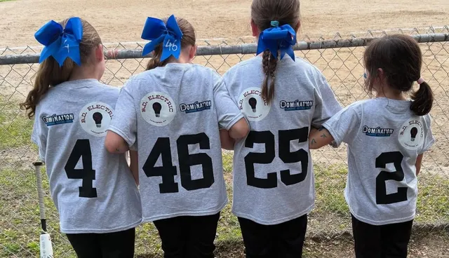 Girl softball players from the Leominster Lassie League standing along fence at local fields.