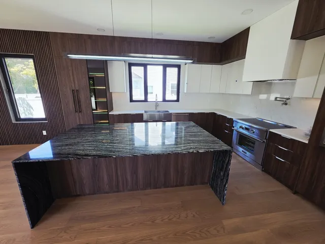 Custom kitchen with walnut cabinetry and a black marble waterfall island, plumbed by IS Plumbing