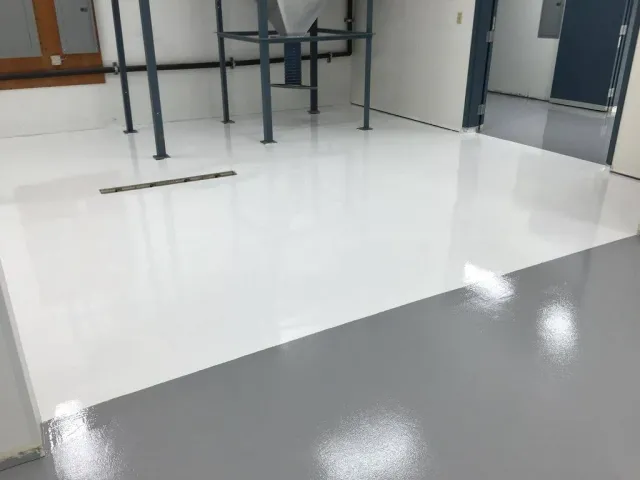 A room with a glossy, two-tone floor, white and gray. Metal supports and a dark doorway are visible.