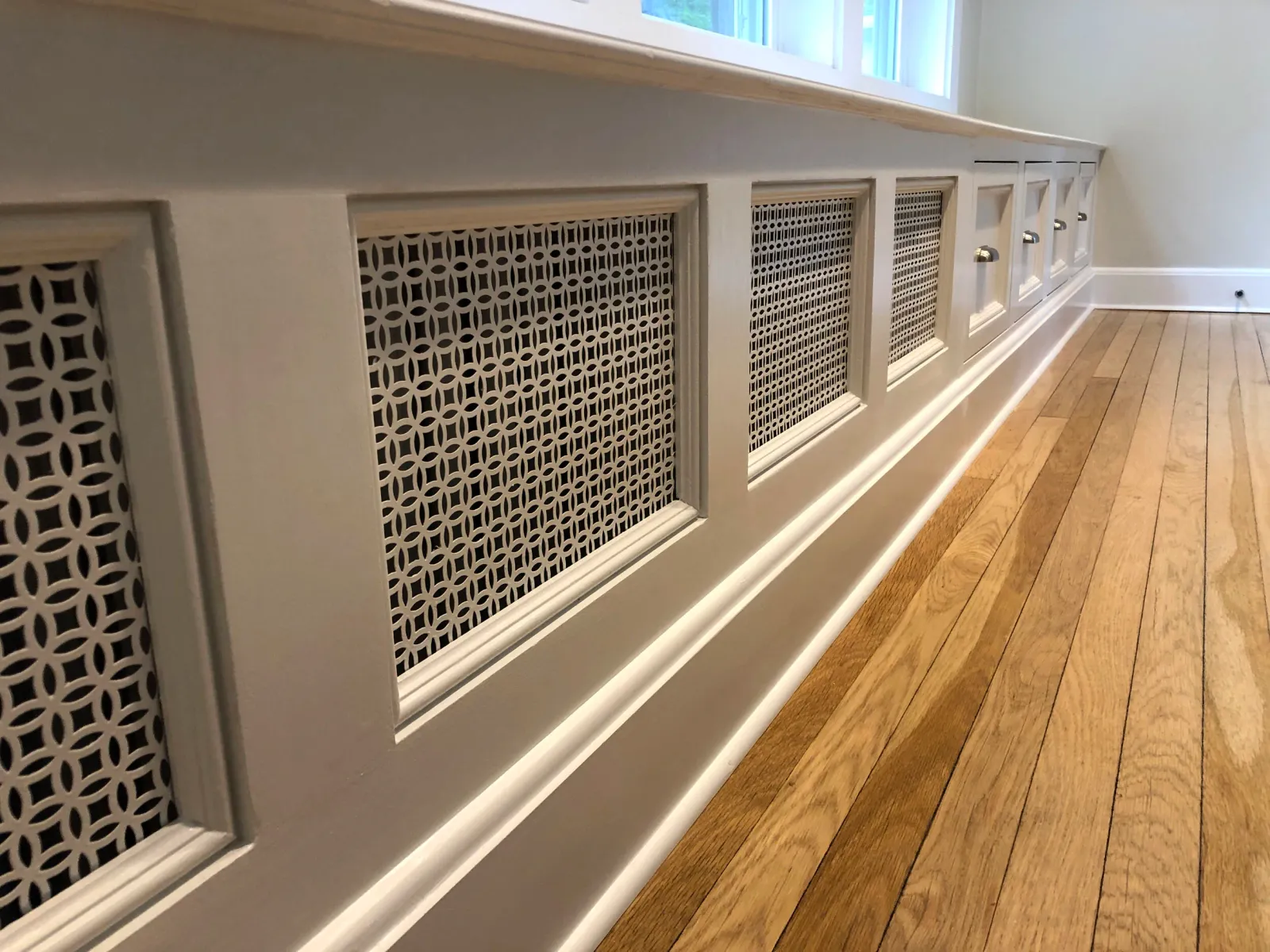 Detail of a massive window seat running the full length of a living room, with storage drawers and vents for a built-in radiator