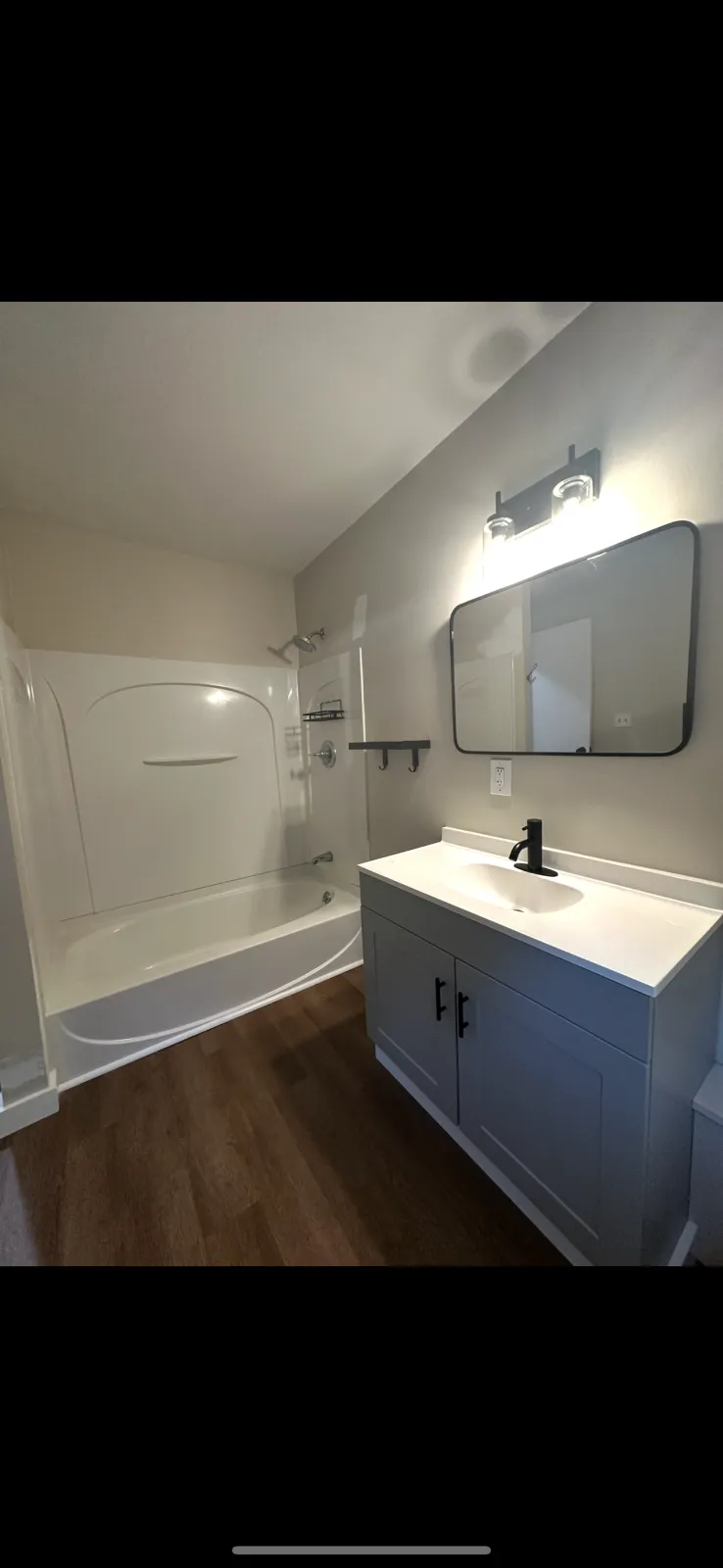 Bathroom with a bathtub and shower combination, a small vanity with a mirror, and wooden flooring.