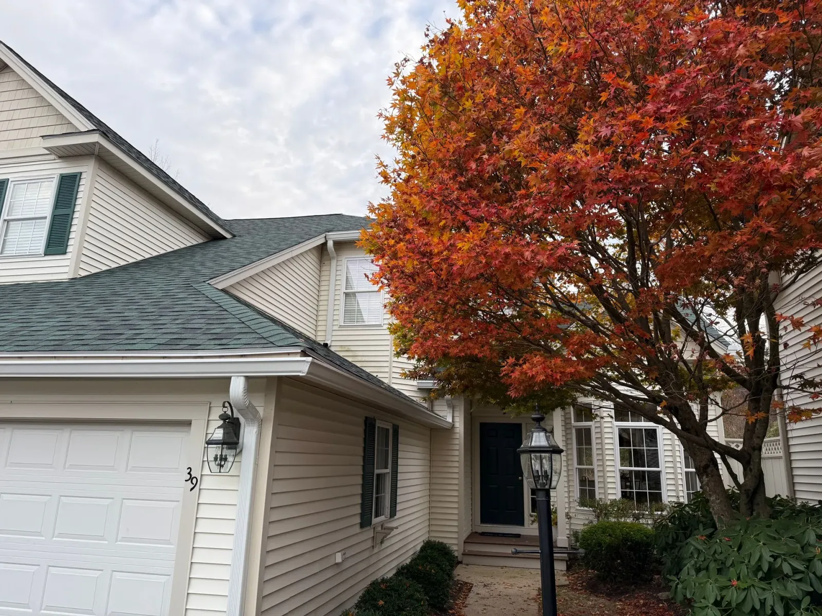 Suburban house entrance with white siding, garage, and a large red-orange autumn tree.