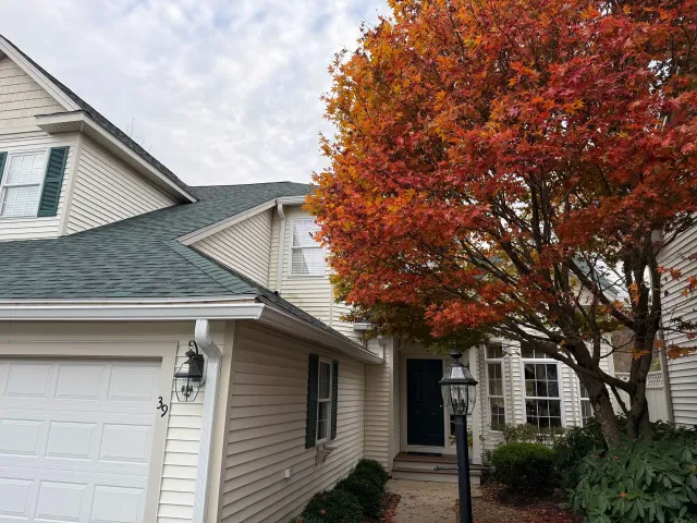 Suburban house entrance with white siding, garage, and a large red-orange autumn tree.