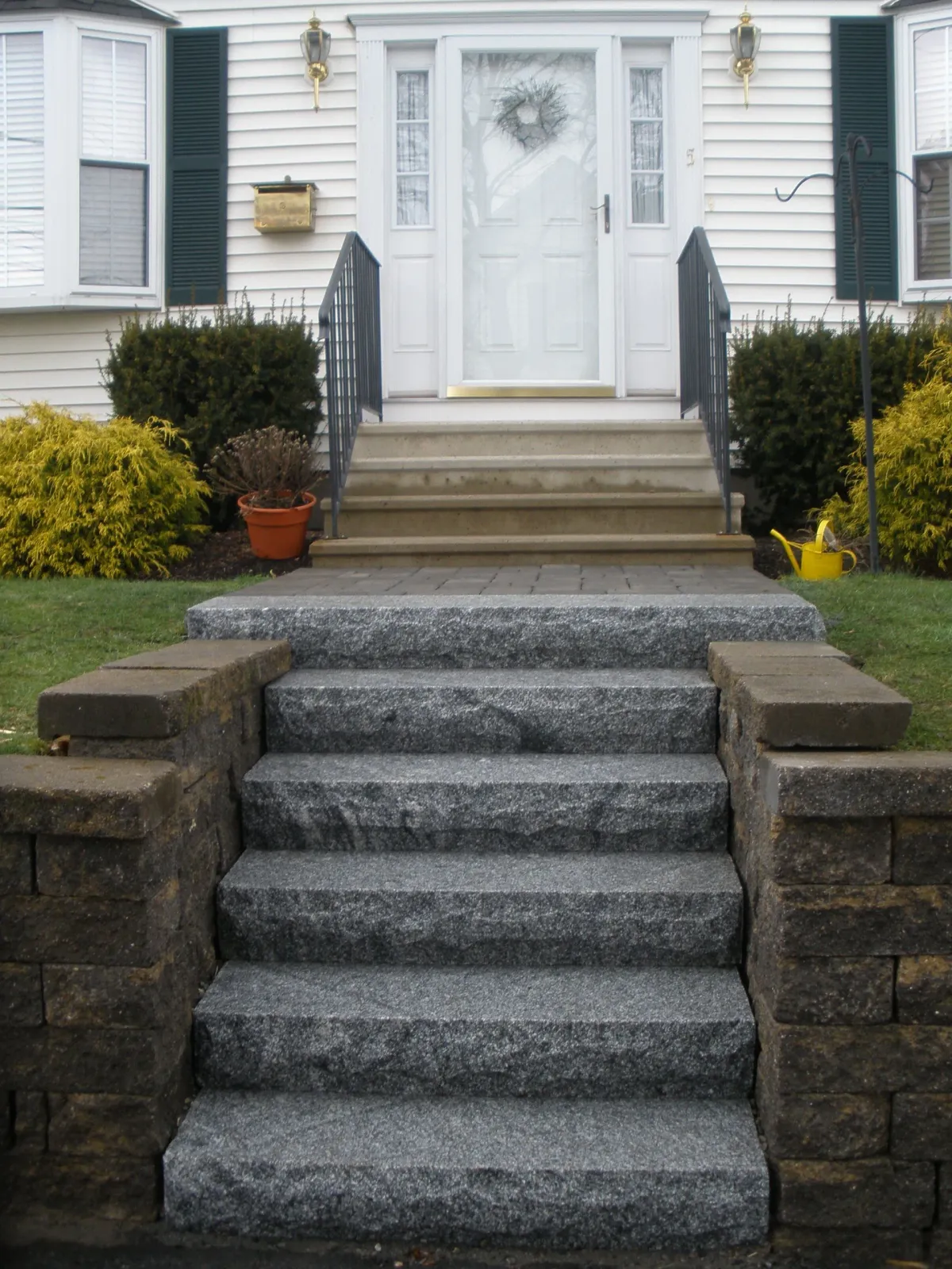 Stone steps leading up to a white house entrance. Granite steps with brick retaining walls.