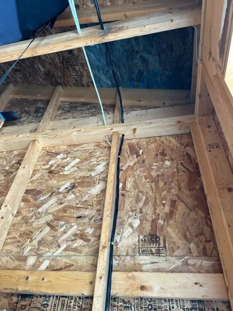 Interior view of a wooden framed wall with black wires running along it. Blue material in the upper right.