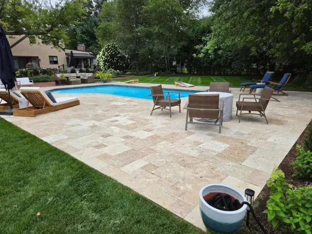Patio with a swimming pool, wicker chairs, and a potted plant in a backyard.