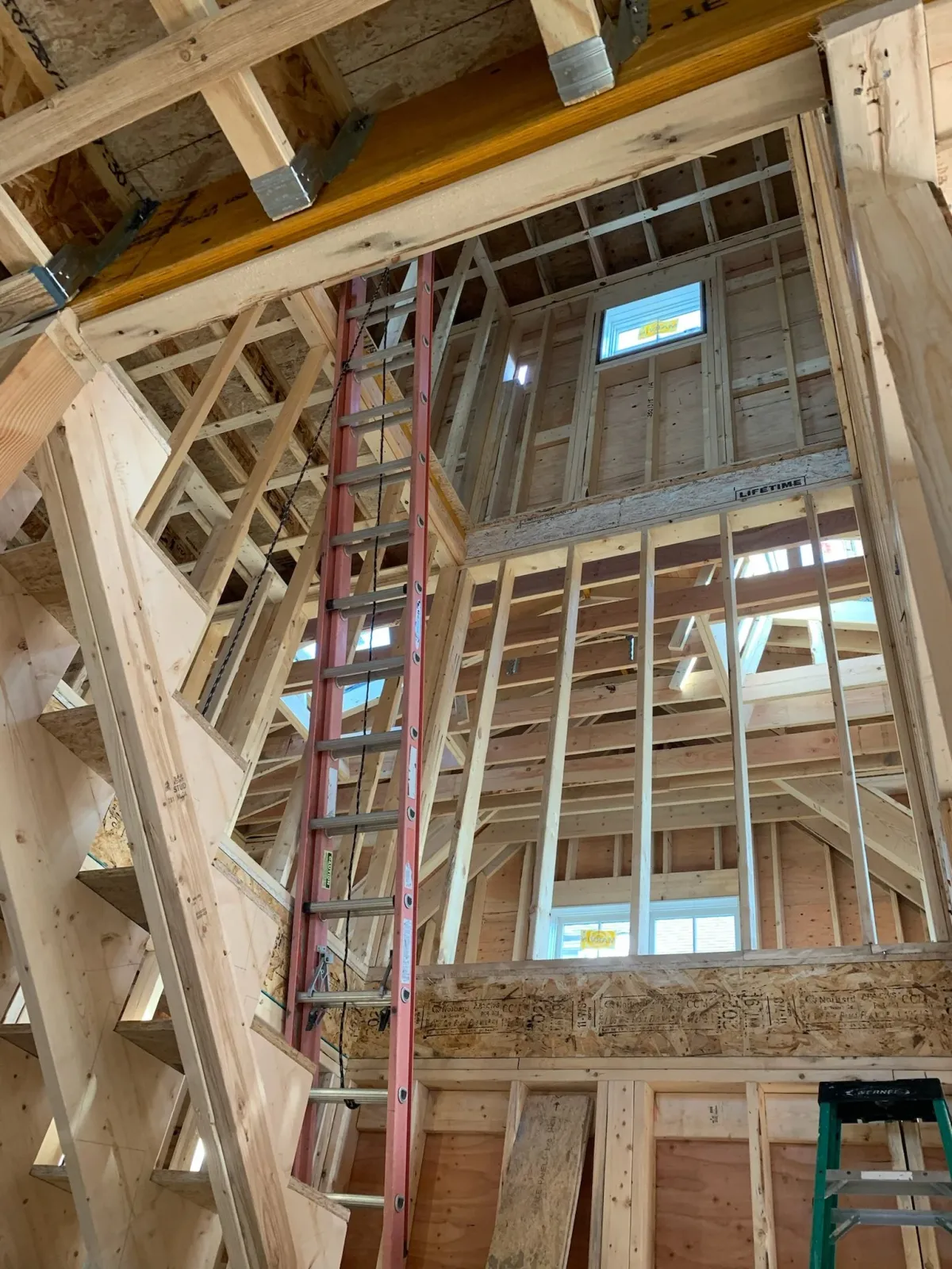 Interior view of a house under construction with wooden framing, a red ladder, and small windows. Scituate, Norwell, Hanover, Hanson, Marshfield, South Shore. Massachusetts Local Construction Company.