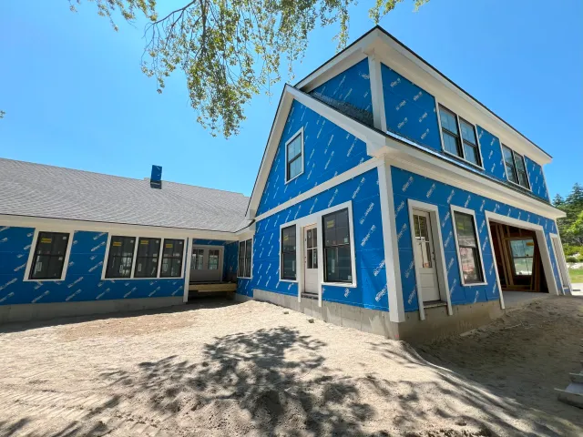 Multi-gabled residential home wrapped in blue Blueskin barrier with black windows and white trim.