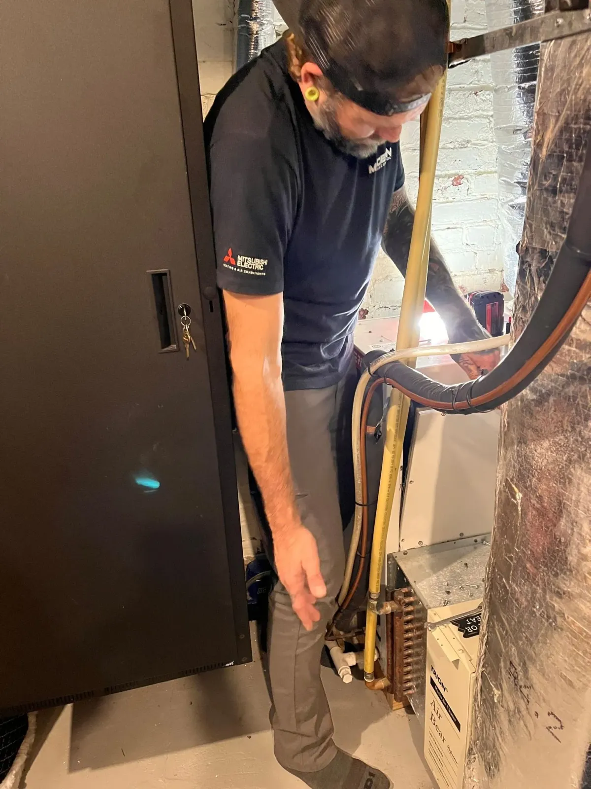 A man is working on an air conditioner in a basement.
