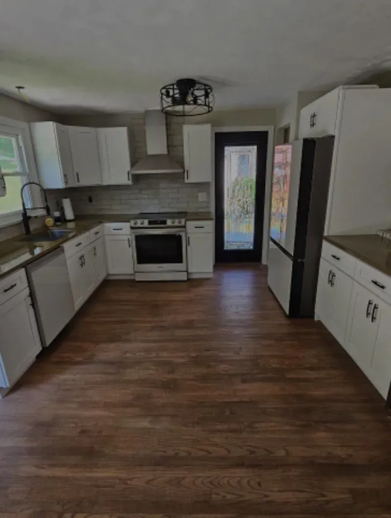 A kitchen with hardwood floors , white cabinets , a stove , a refrigerator , and a sink.