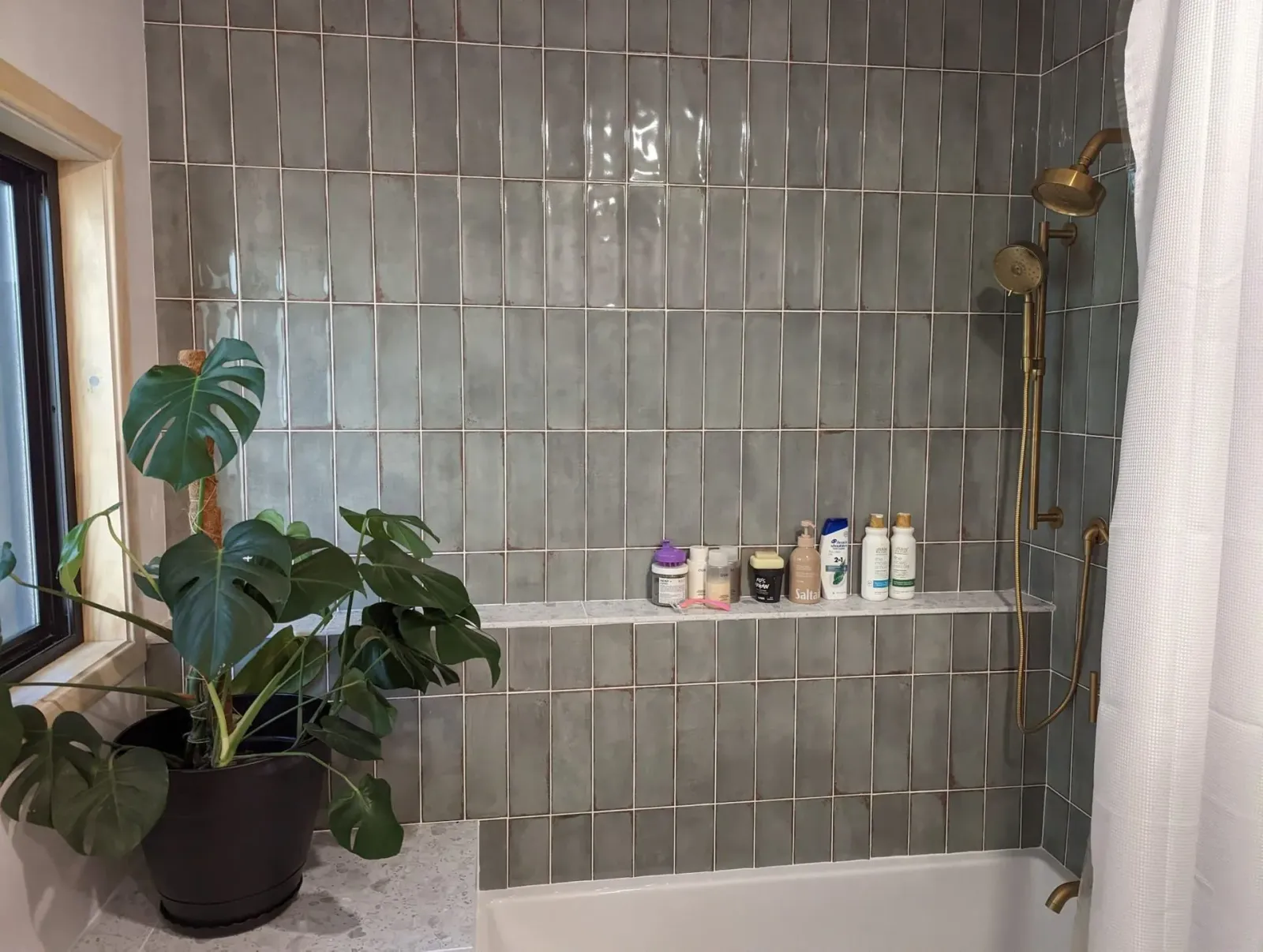 A bathroom with a shower, tub, shelf and window.