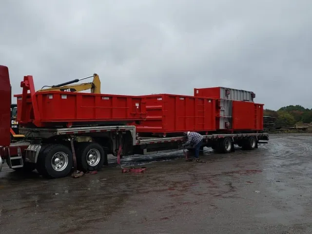 Red flatbed truck trailer parked on a wet lot under a cloudy sky