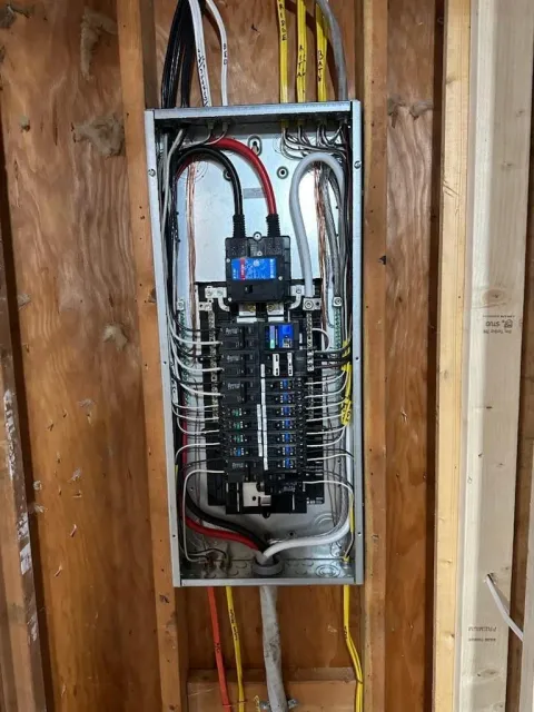 Open electrical breaker panel mounted in unfinished wood wall with exposed wiring