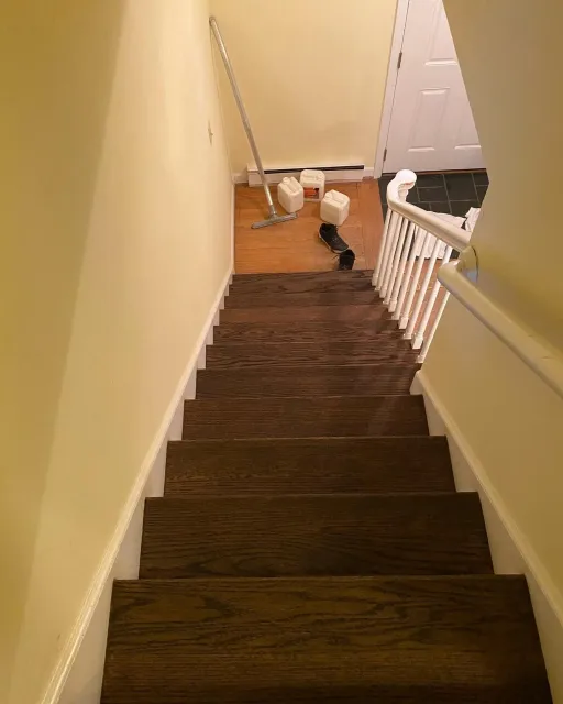 Staircase with dark brown steps, white railing, and beige walls; supplies at the bottom.