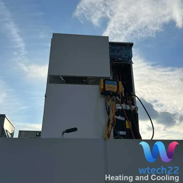 HVAC unit on a rooftop being serviced with a yellow gauge. Blue sky background.