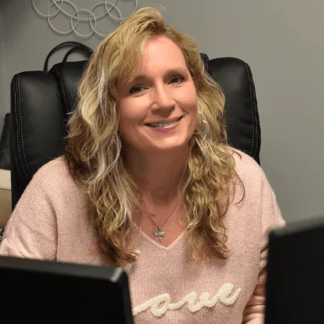 Smiling woman with wavy blonde hair sitting in an office chair.