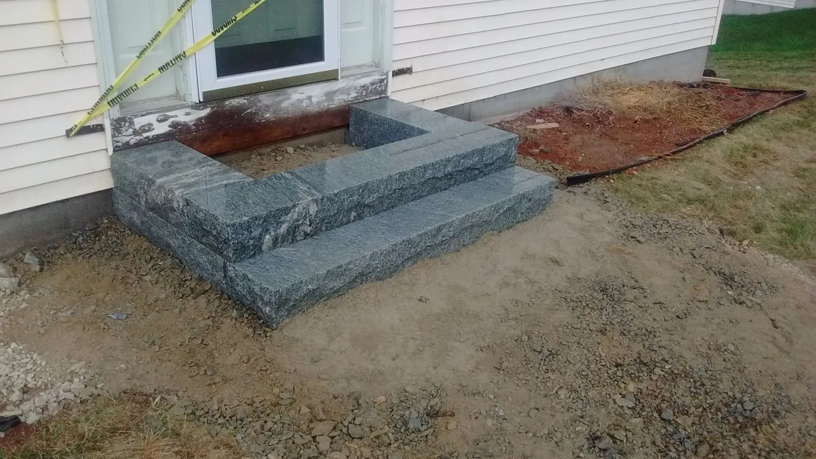 Partially constructed granite steps in Webster, MA, surrounded by gravel, dirt, and caution tape, showcasing the progress of the entry renovation. Project by KRD Landscaping.