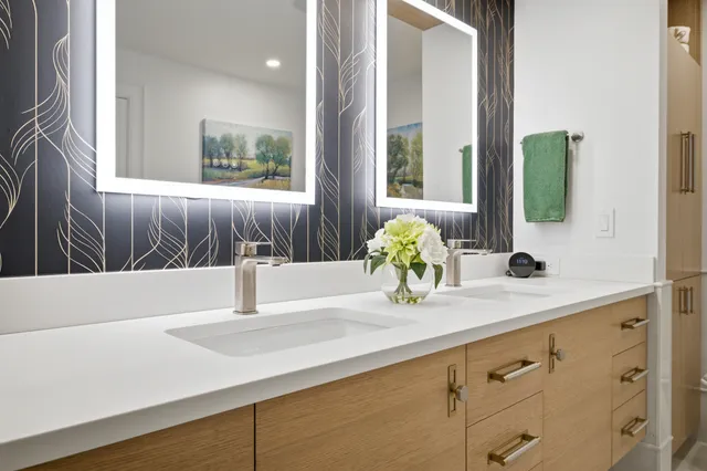 Braintree primary bath with a rift sawn white oak floating vanity, white quartz counter, dark botanical wallpaper, and LED mirrors.